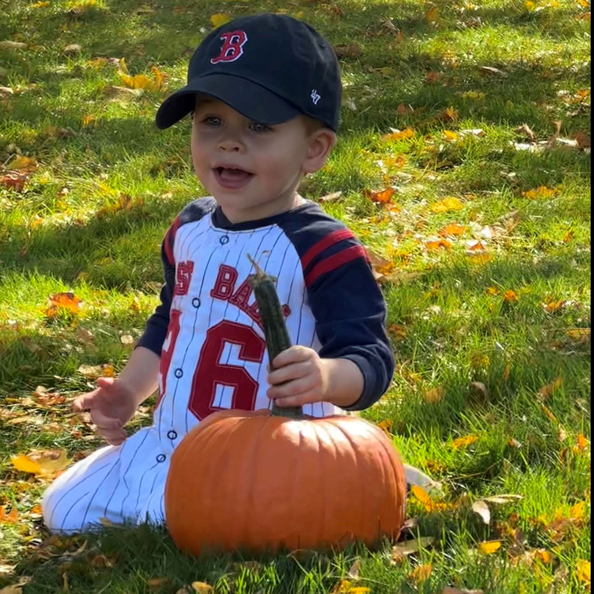 young boy in baseball costume holding a pumpkin