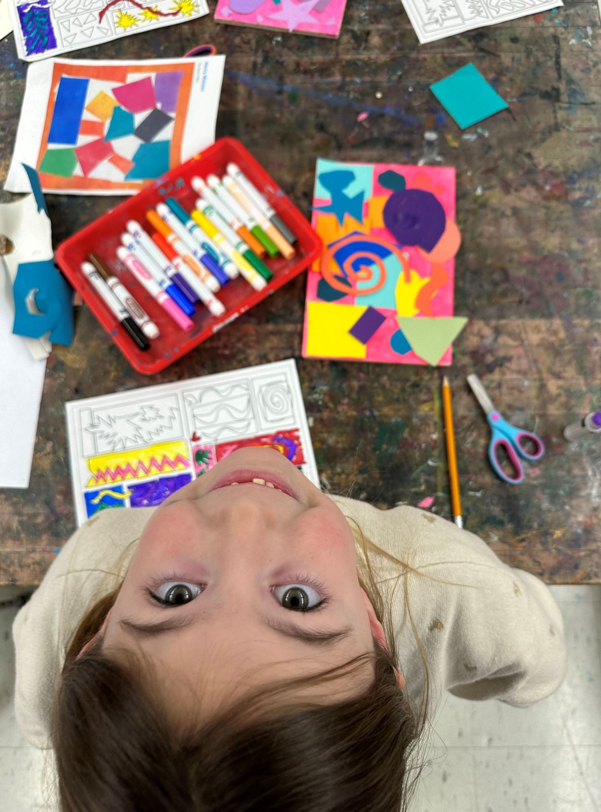 Photo of child looking up at camera while finishing art project